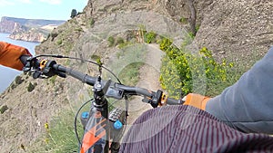 Point chest view from action camera e-bike handlebar and hands while riding on cliff edge trail along sea. Bicyclist holding handl