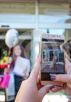 .Point of view of a person taking a photo with a smartphone of a girl holding flowers and a diploma. Graduation celebration,