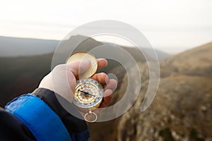Point of view photo of explorer man searching direction with golden compass in his hand with autumn mountains background