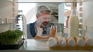 Point of view POV from inside refrigerator fridge middle-aged Caucasian man at home kitchen unpack products goods to