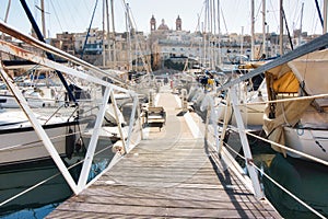 Point-of-view shot from the entrance of a wooden jetty pier leading to harbored yachts in a marina