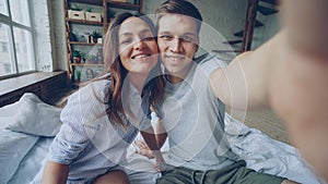 Point of view shot of loving couple taking selfie together posing having fun while sitting on bed at home. Nice modern