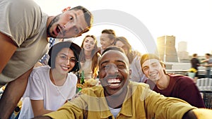 Point of view shot of young people multiethnic group taking selfie and holding camera, men and women are looking at