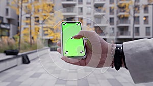Point of view of successful man using phone with green mock-up screen near office building