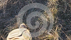 Point of view to female feet of ukrainian soldiery going in brown boots through dry grass at countryside. Legs of young