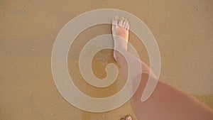 Point of view of young woman stepping at the golden sand at sea beach. Female legs walking near ocean. Bare foot of girl