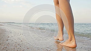 Point of view of young woman stepping at the golden sand at sea beach. Female legs walking near ocean. Bare foot of girl going on