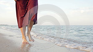 Point of view of young woman stepping at the golden sand at sea beach. Female legs walking near ocean. Bare foot of girl going on