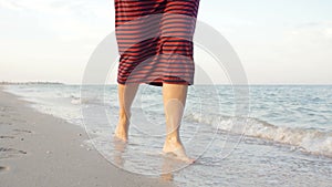 Point of view of young woman stepping at the golden sand at sea beach. Female legs walking near ocean. Bare foot of girl going on