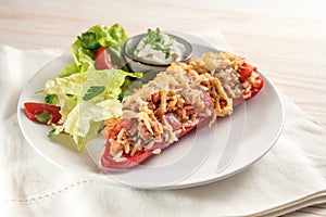 Pointed bell pepper baked with rice, tuna, tomatoes and cheese, lettuce salad, and dip, on a white plate and napkin, bright wooden