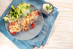 Pointed bell pepper stuffed with rice, tuna, tomatoes and cheese on a blue plate with lettuce salad, and dip, on a napkin and a