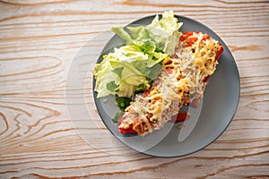 Pointed red bell pepper baked with rice, tuna and cheese, lettuce salad with parsley garnish on a gray blue plate, rustic wooden