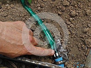 pointing a finger at flowing water from a drip irrigation hole in the soil