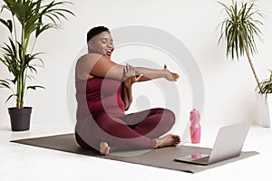 Poisitive plus size woman doing stretching in front of laptop