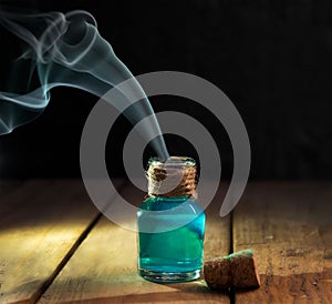 Poison with smoke in magic bottle on black and wooden background. Selective focus