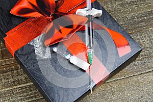 Poisoned chalice gift symbol concept: isolated syringe with injection needle and vial with white fluid on present box on wood