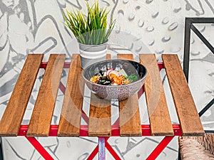 Poke bowl with avocado, radish, salmon, corn, seaweed, peas, nori, daikon, sesame seeds in a black plate on small wooded table