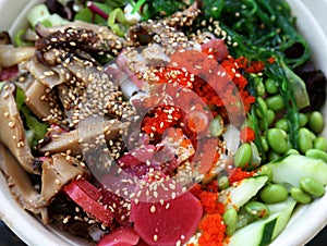 poke bowl colorful detail with cucumber, octopus, masago, seaweed salad, edamame, soy beans, ponzu sauce, salmon)