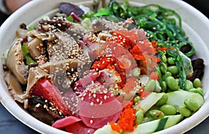 poke bowl colorful detail with cucumber, octopus, masago, seaweed salad, edamame, soy beans, ponzu sauce, salmon)