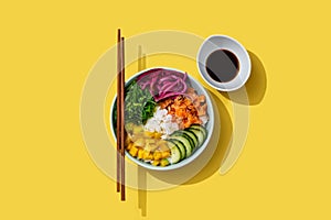 Poke bowl with rice, salmon,cucumber,mango,onion,wakame salad, poppy seeds ands sunflowers seeds on yellos background