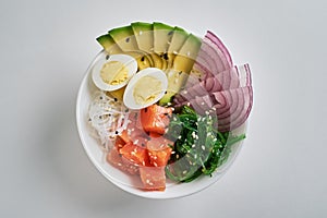 poke bowl with salmon, avocado, rice, Chuka Salad, sweet onions, quail eggs sprinkled with white and black sesame isolated on