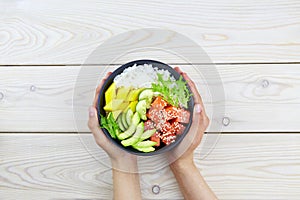 Poke bowl of salmon, rice, avocado, cucumber, mango, herbs in a woman's hands. Hawaiian ahi, a diet meal with fish