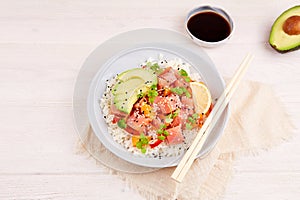 Poke bowl with salmon, rice, avocado, micro greens, pepper and soy sauce on white wooden background.