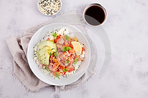 Poke bowl with salmon, rice, avocado, sesame seeds, micro greens, pepper and soy sauce on grey backround
