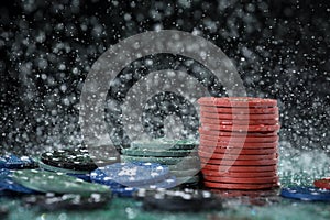 Poker playing chips on a green table and black background under the water drops. Online gambling.