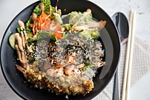 PokÃ© bowl with flambÃ© salmon, Tempura shrimp, guacamole, Masago caviar, salad and sesame on rice and black porcelain plate