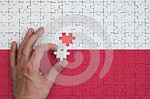 Poland flag is depicted on a puzzle, which the man`s hand completes to fold