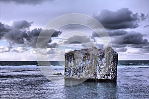 Pole in ocean. Rock with vertical walls. Basaltic parting,