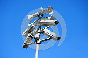 A pole on the street with cameras and loudspeakers mounted on it against a blue sky background