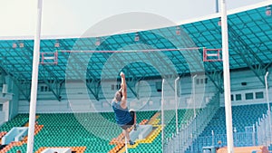 Pole vault training - an athletic man jumping over the bar in the stadium