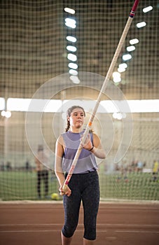 Pole vaulting - young woman in purple shirt raised a long pole