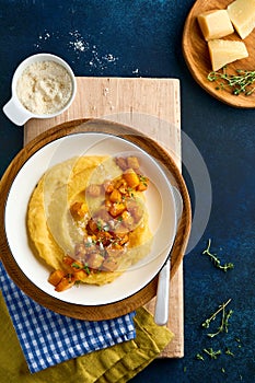 Polenta with butter, pumpkin, garlic, savory and parmesan cheese in white bowl on dark blue concrete background. Traditional Basic