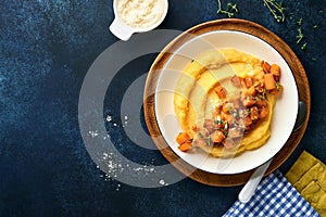 Polenta with butter, pumpkin, garlic, savory and parmesan cheese in white bowl on dark blue concrete background. Traditional Basic