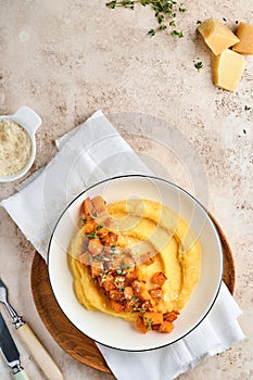 Polenta with butter, pumpkin, garlic, savory and parmesan cheese in white bowl on light concrete background. Traditional Basic