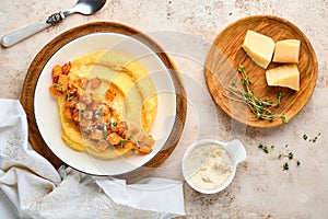 Polenta with butter, pumpkin, garlic, savory and parmesan cheese in white bowl on light concrete background. Traditional Basic