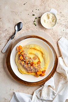 Polenta with butter, pumpkin, garlic, savory and parmesan cheese in white bowl on light concrete background. Traditional Basic