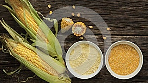 Polenta corn grits and corn flour in a porcelain bowl on a wooden table. Ears of corn and pieces of corn next to bowls. Gluten