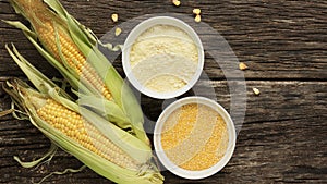Polenta corn grits and corn flour in a porcelain bowl on a wooden table. Ears of corn and pieces of corn next to bowls. Gluten