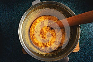 Polenta or mamaliga and beech wood stirrer in cast iron pot cooper pot. Traditional dish prepared by boiling water, salt,