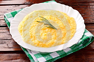 Polenta in white dish on rustic wooden table. Cream of corn or mamaliga