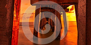 Poles of the beautiful Old Naples Pier over water in Florida at sunset