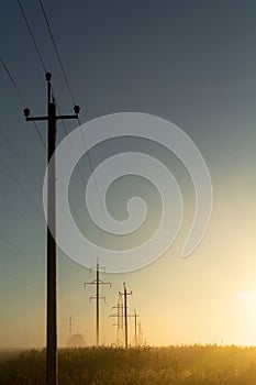 Poles with high-voltage wires are illuminated by the dawn sun in the field of infinity theme Creation