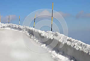 poles painted yellow and black stuck in the snow to delimit the edge of the icy mountain road