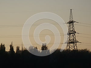 Poles with wires that transmit high-voltage current. Background of the evening sky with the sun