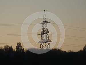 Poles with wires that transmit high-voltage current. Background of the evening sky with the sun