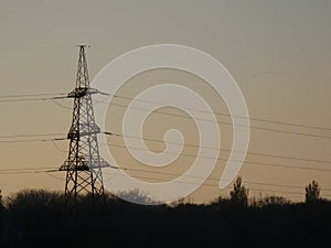 Poles with wires that transmit high-voltage current. Background of the evening sky with the sun